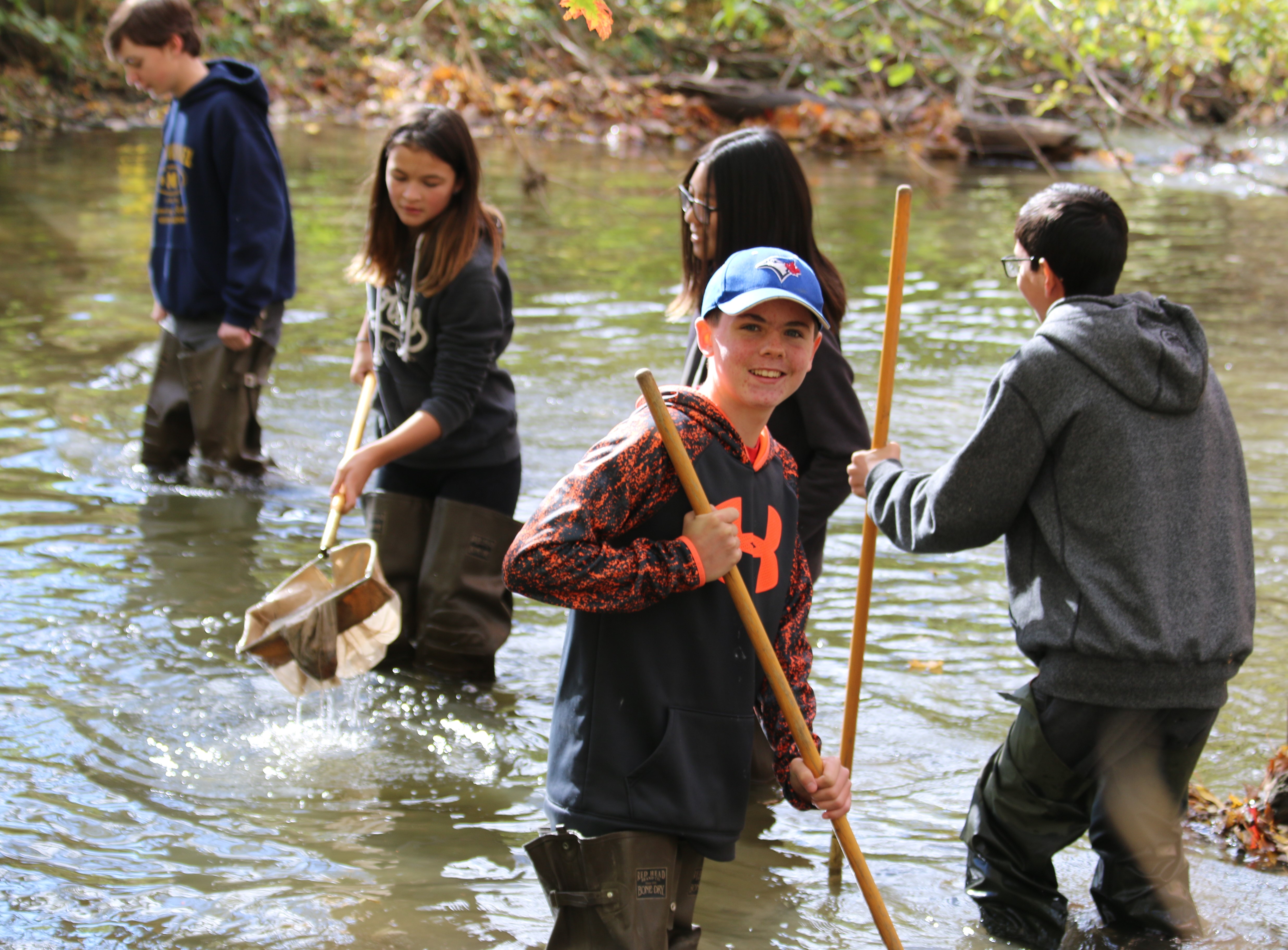 Students wearing hip waders stand in a stream with nets