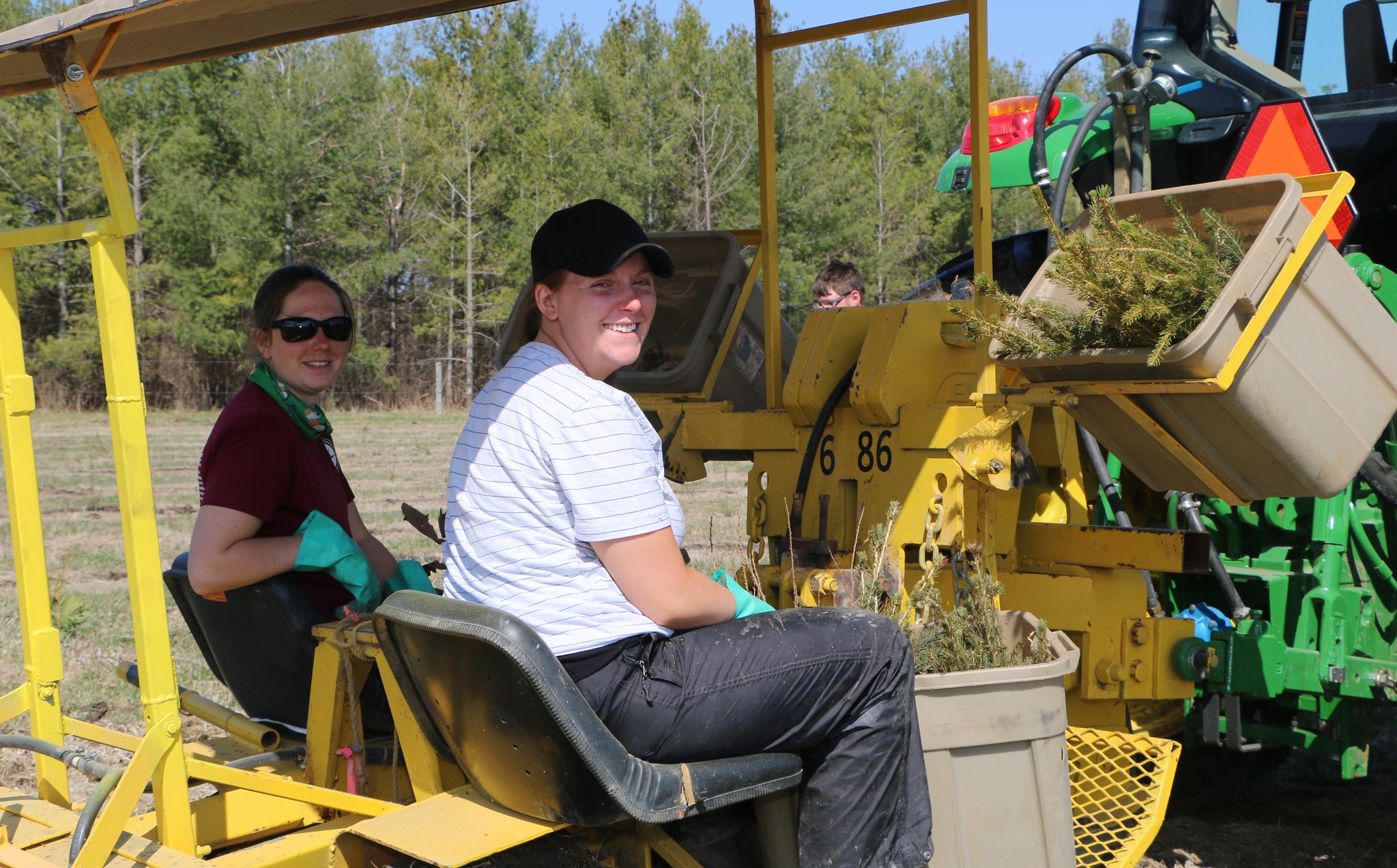 Two people are seated on a tree planting machine.