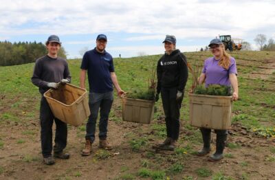 Four people standing with totes of trees about to be planted