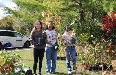 Three students hold potted trees