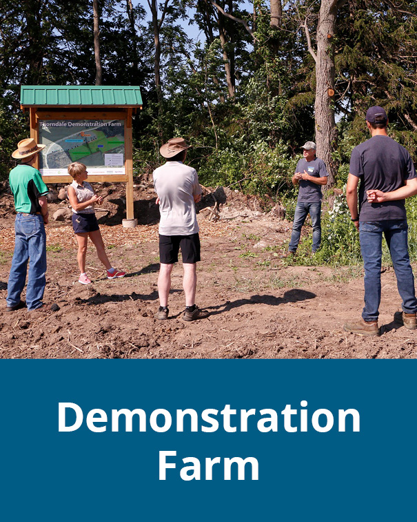 People stand in a circle in front of a sign about the Thorndale Demonstration Farm.