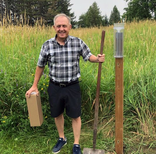Person stands next to a rain gauge, in a field