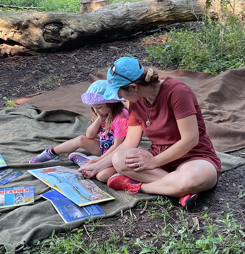 Child and caregiver reading a book in the woods during Nature School