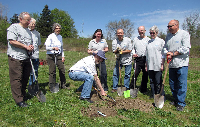 Group of people gathered around person planting a tree in a field