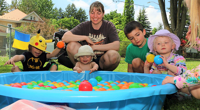Children and an adult gather around a plastic wading pool filled with colourful plastic balls