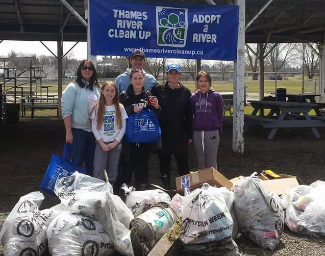 Group of people stand behind pile of garbage bags of trash collected during a previous Thames River Clean Up