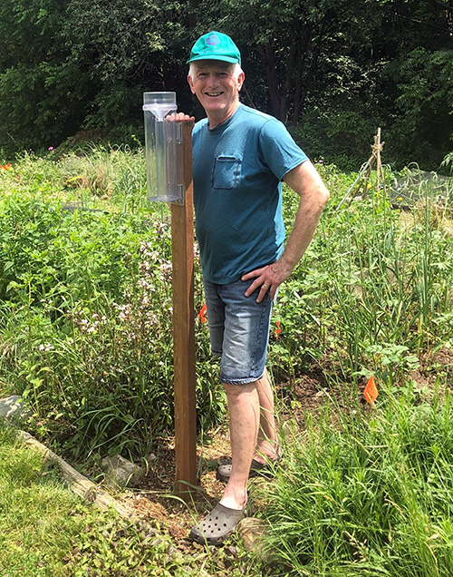 Person stands next to a rain gauge in his garden