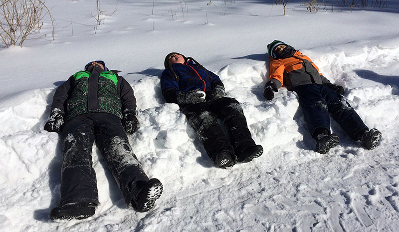 Three children lie in the snow on a Nature School outing