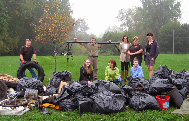 People stand next to pile of bagged garbage and other trash that they have picked up in a large park