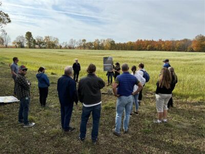 Attendees stand in a field listening to presentation
