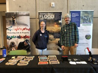 Two educators stand in front of three pull up banners and an information table