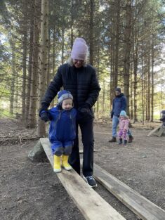 A caregiver helps a toddler walk on a balance beam