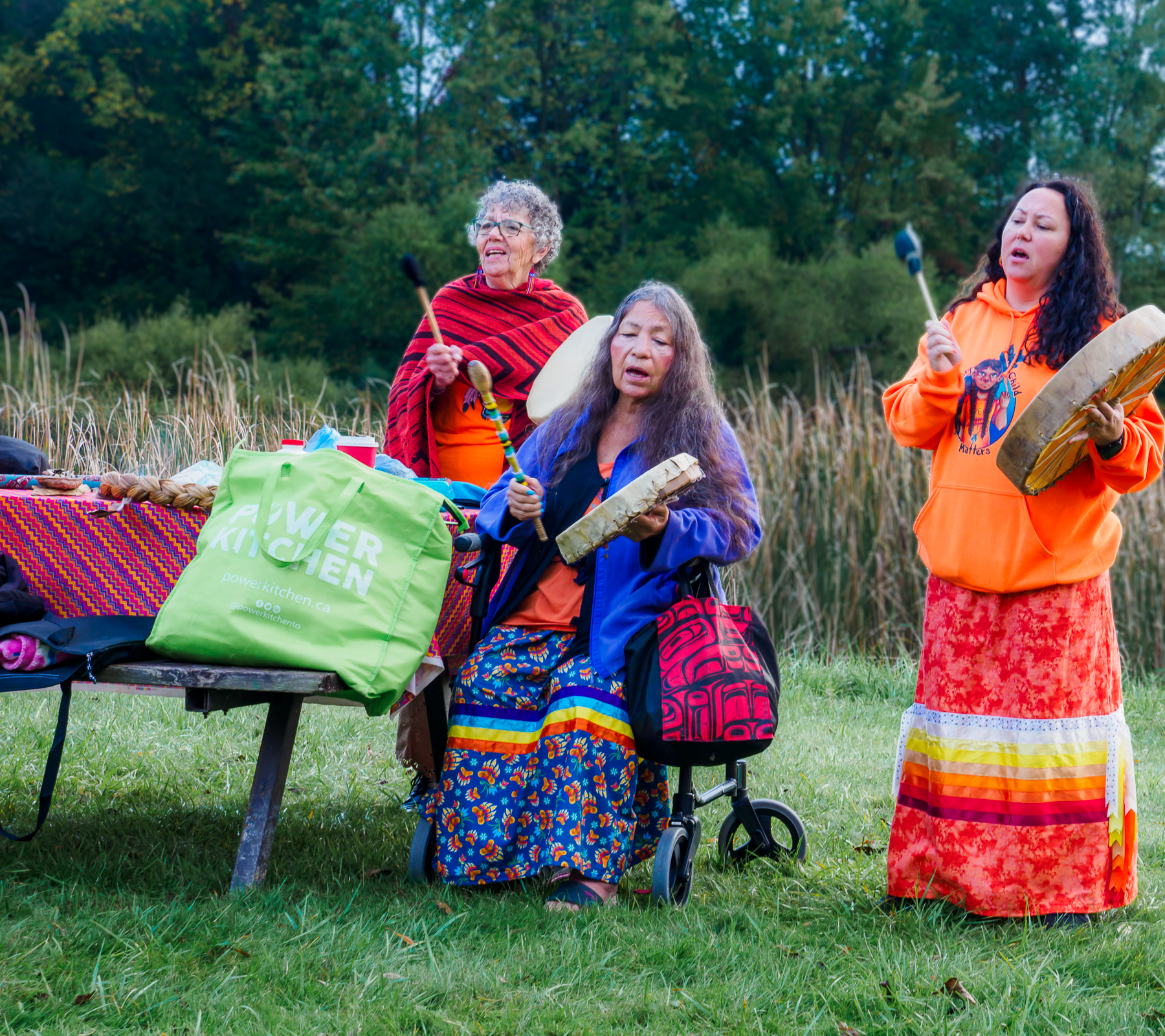 Women play hand drums outside.