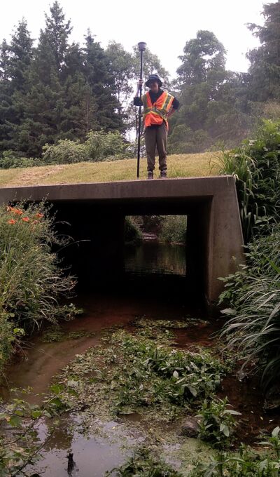 A staff stands on a bridge holding surveying equipment