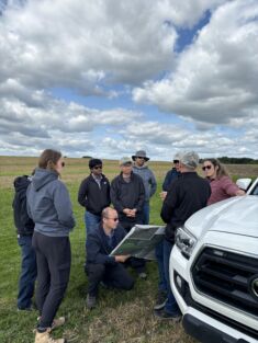 A group of people look over a map in a agricultural field