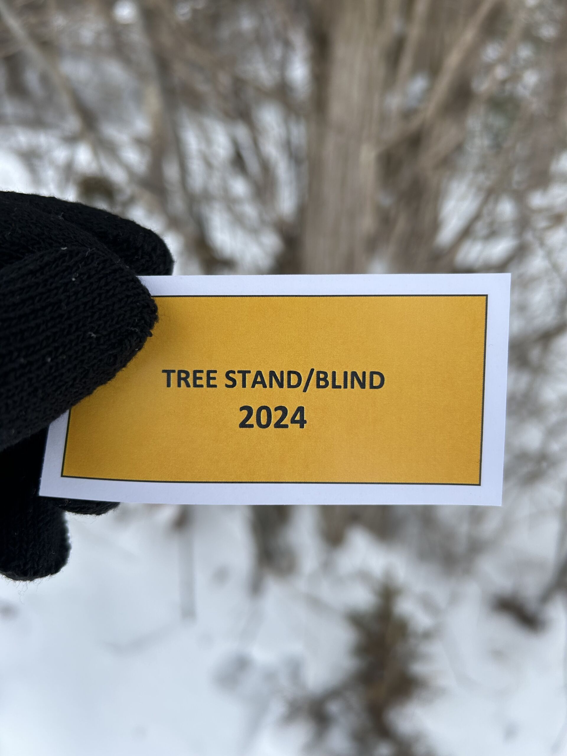 A gloved hands holds a piece of paper that says Tree Stand/Blind 2024
